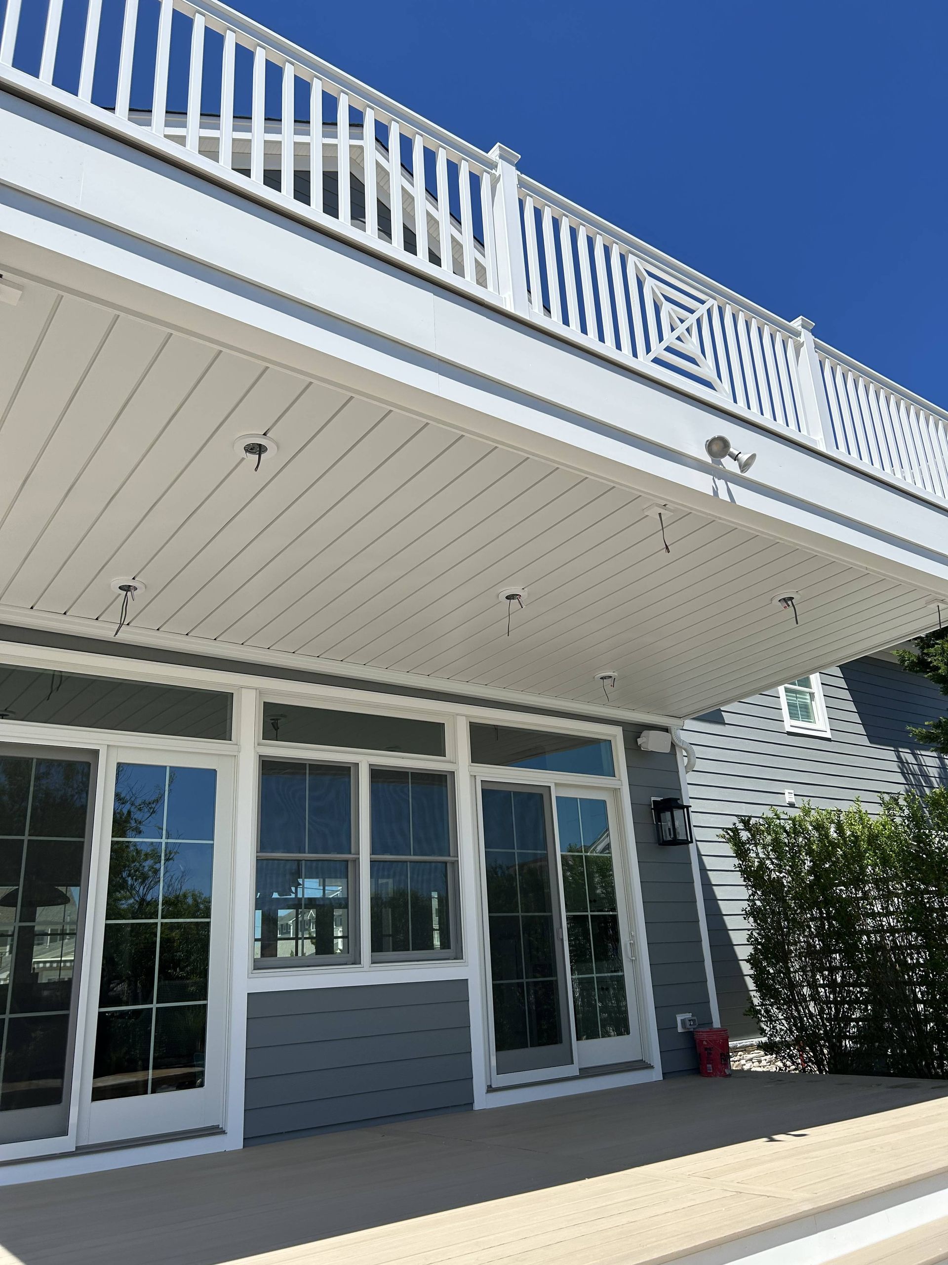 White beach house porch with glass doors, blue railings, and potted greenery under a clear sky