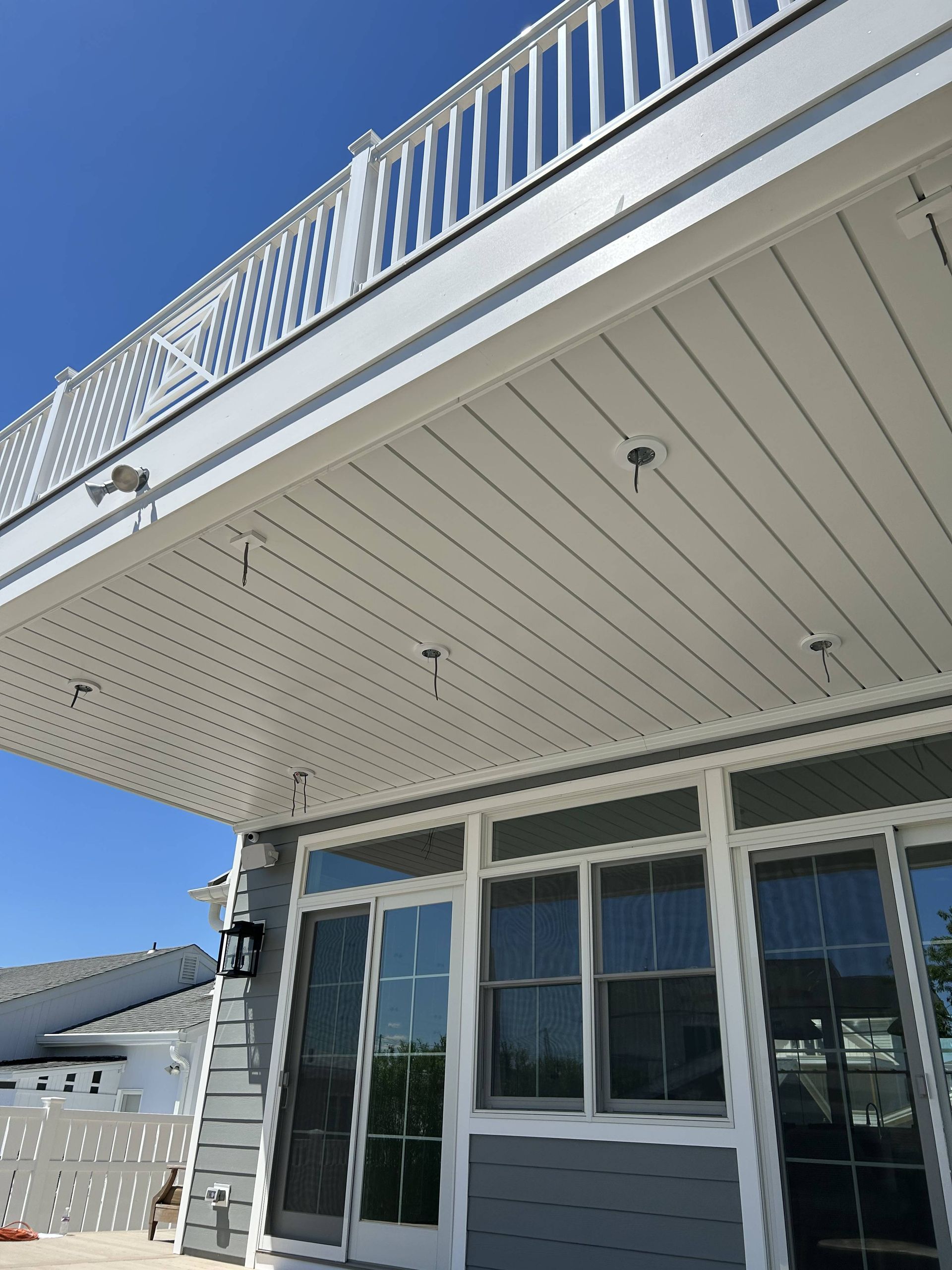 White house exterior with balcony, siding, and large windows under a clear blue sky