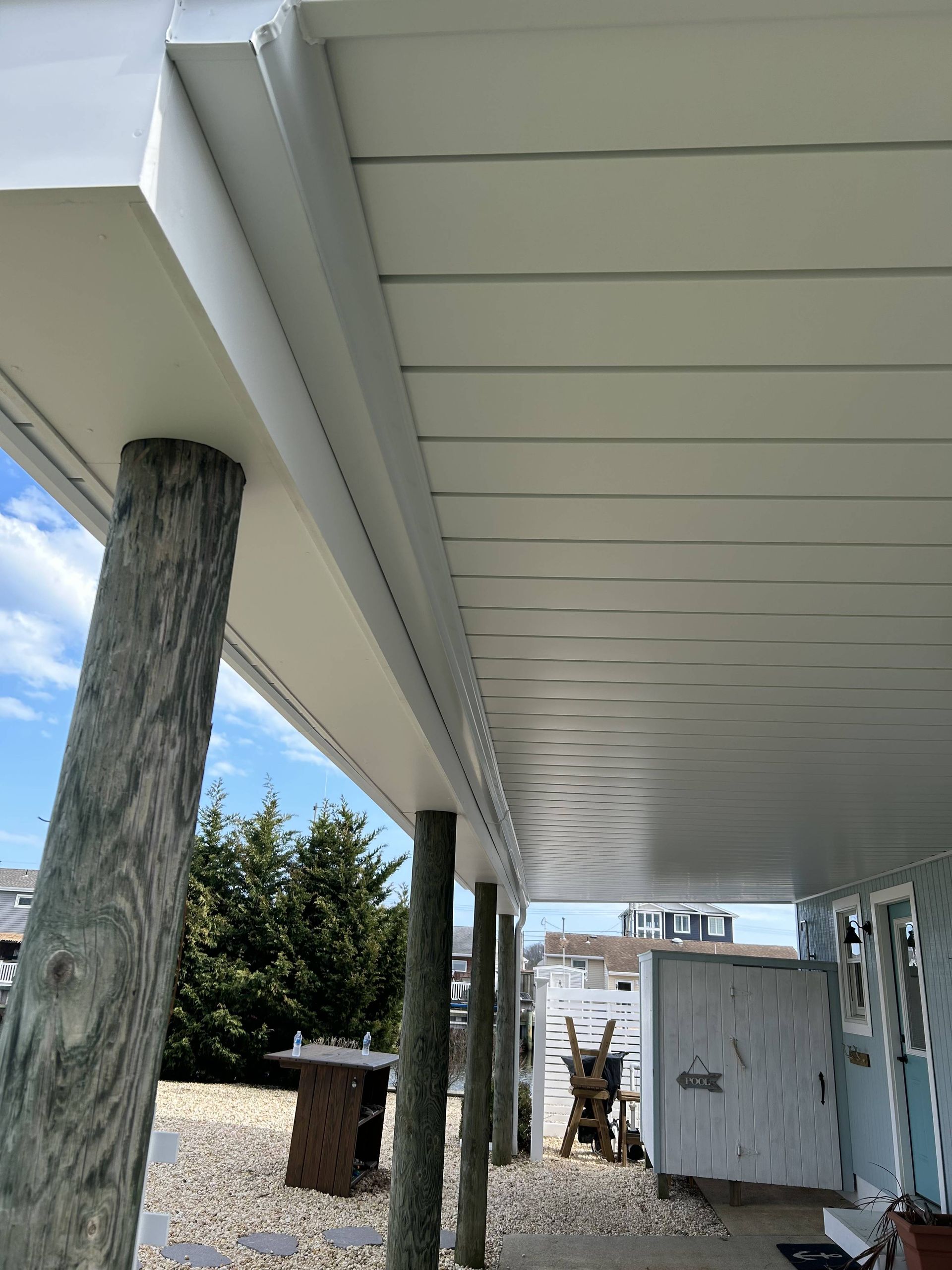 Under-stilt house walkway with white ceiling, wooden posts, and beach gear beside a storage shed