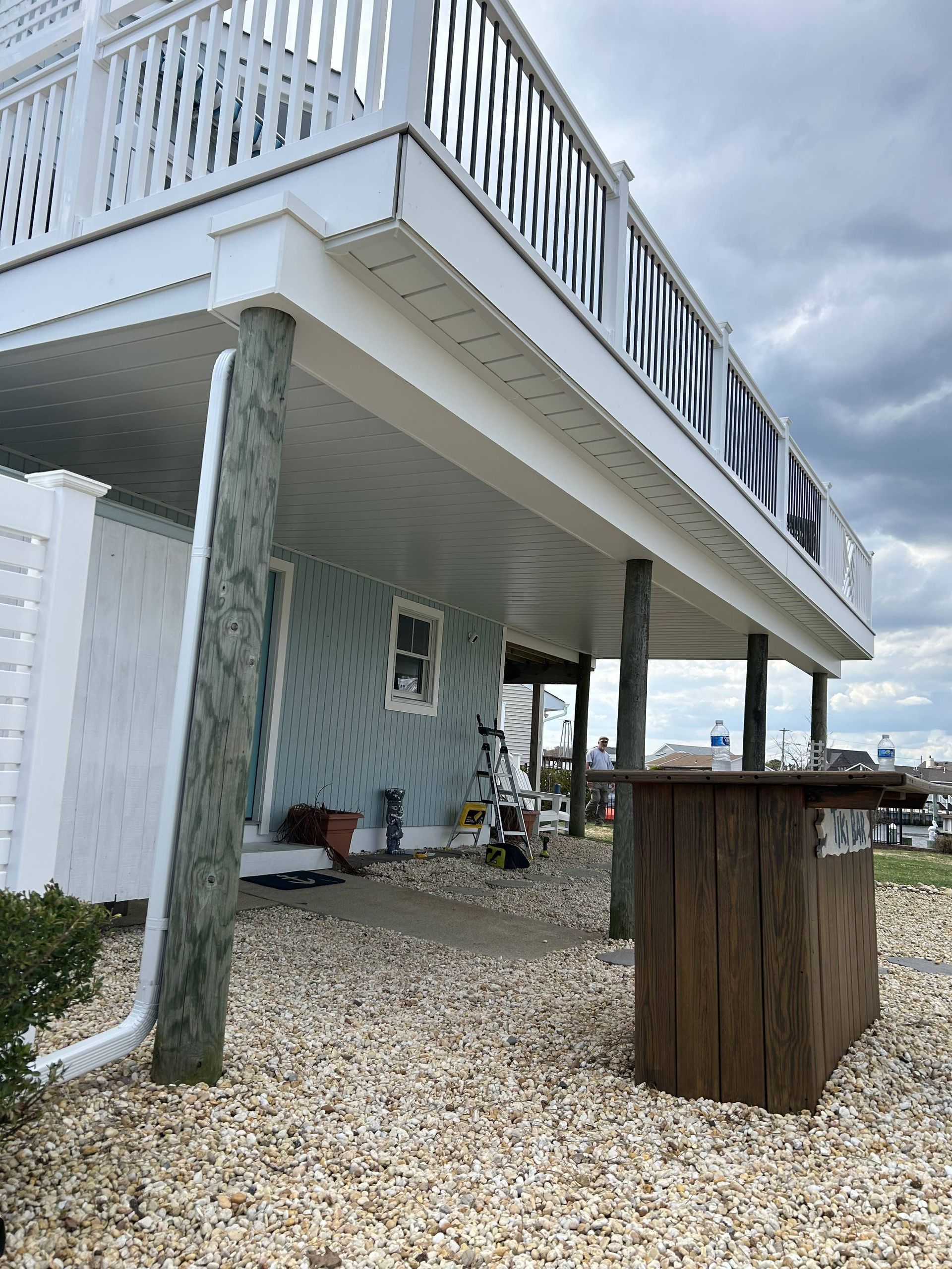 Raised white beach house on stilts above a gravel yard under cloudy skies