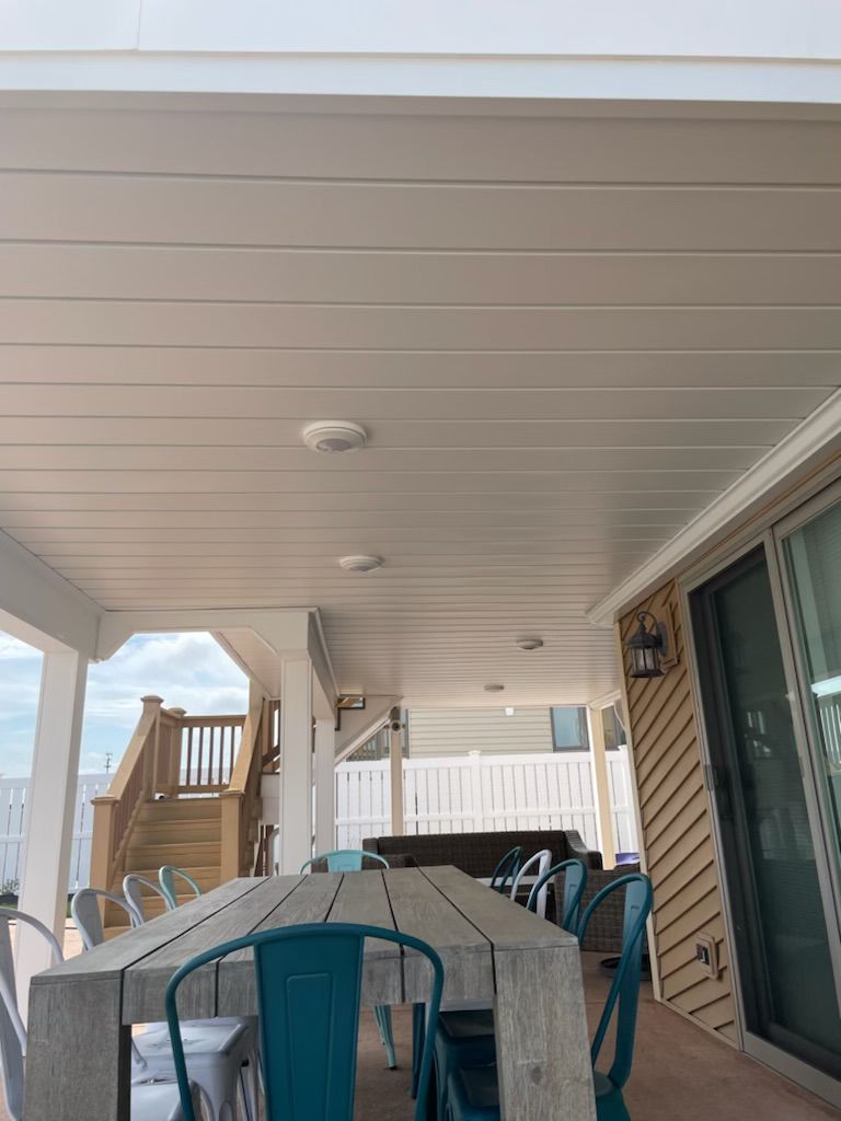 Covered patio with dining table, chairs, and a grill beside a house exterior.