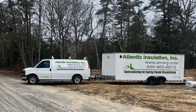 White work van and trailer for Atlantic Insulation, Inc. parked on a dirt road.