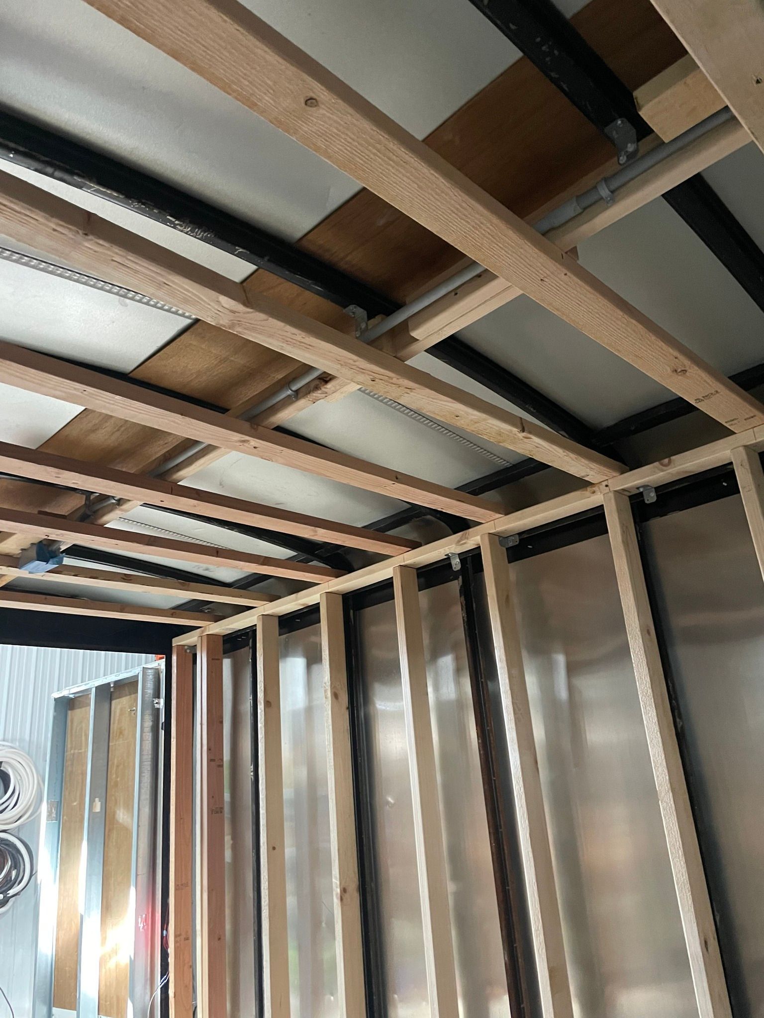 Interior framing of a small trailer or van with exposed wooden studs and metal roof ribs