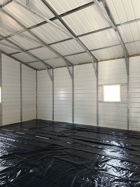 Empty metal shed interior with corrugated walls, arched roof, and black plastic floor covering