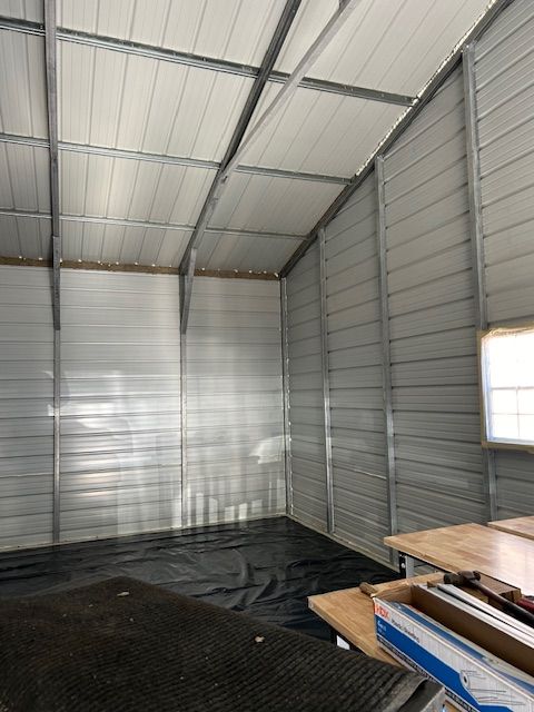 Empty metal shed interior with corrugated walls, white ceiling, and stacked materials in the corner