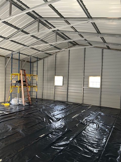 Empty metal warehouse interior with black floor covering, ladder, and two small windows on the wall
