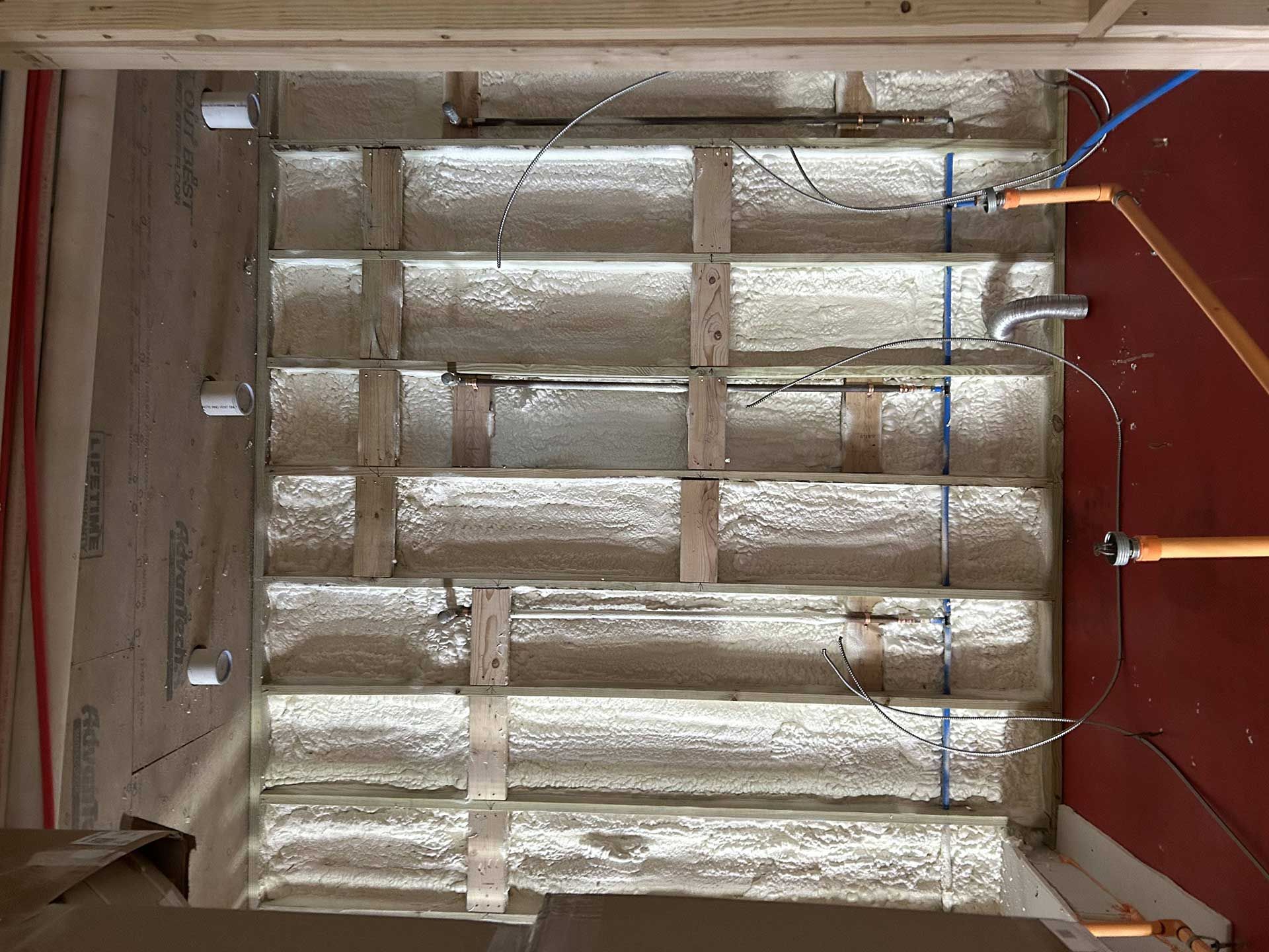Wall framing with insulation, electrical wiring, and plumbing pipes visible in an unfinished room.