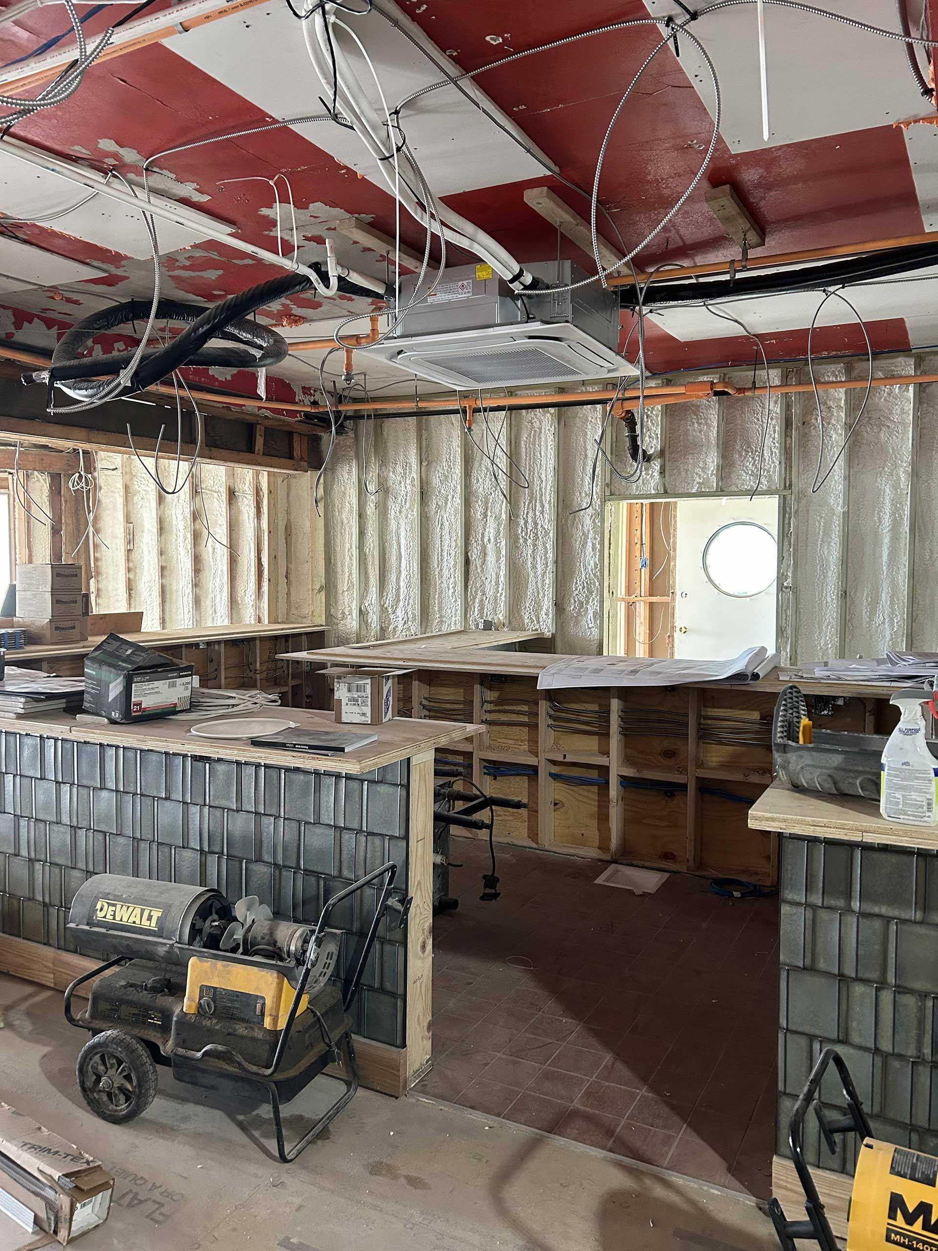 A construction site interior featuring walls with exposed insulation, unfinished ceiling, and a grey tile-covered counter.