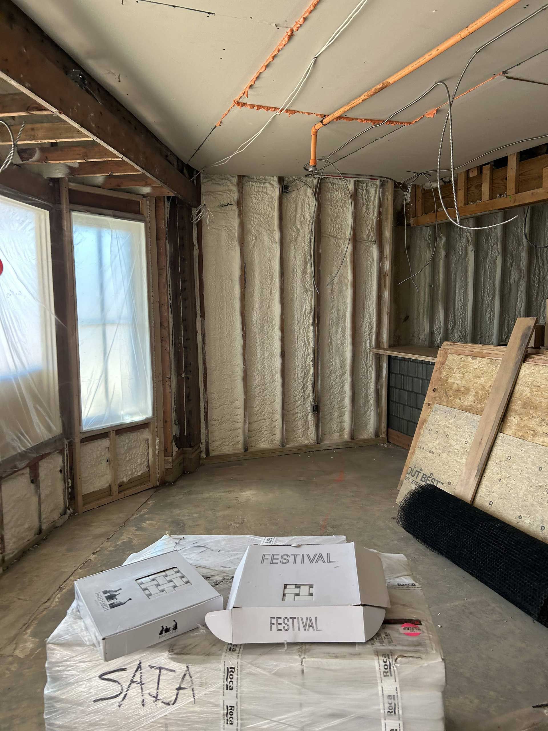 Interior view of a room under construction with spray foam insulated walls and construction materials stacked in the front.