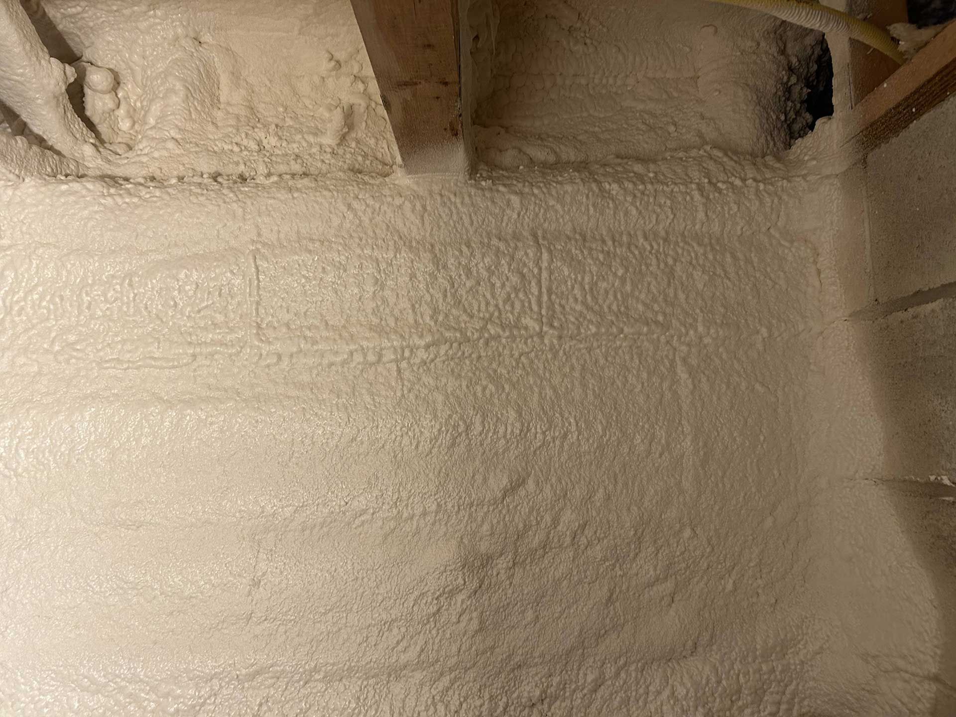 Spray foam insulation applied to the underside of a wooden floor joist assembly.