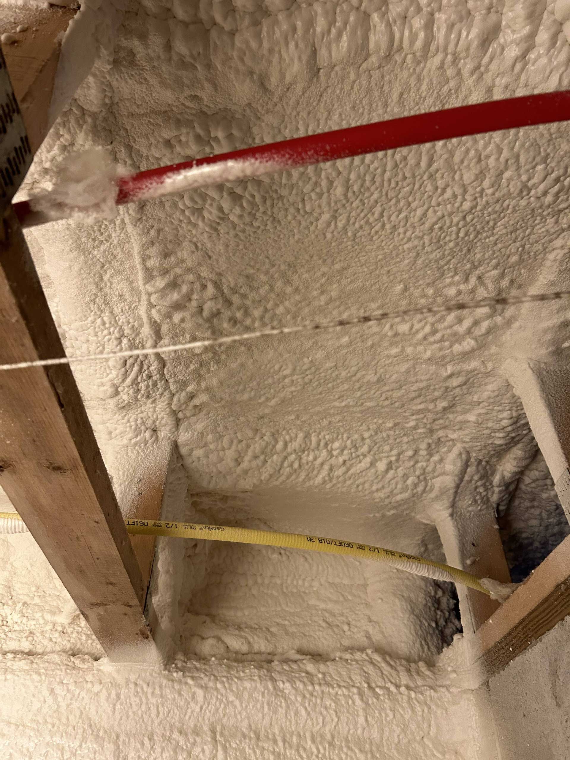 View looking up at wooden ceiling joists and underside of roof deck coated in white spray foam insulation.