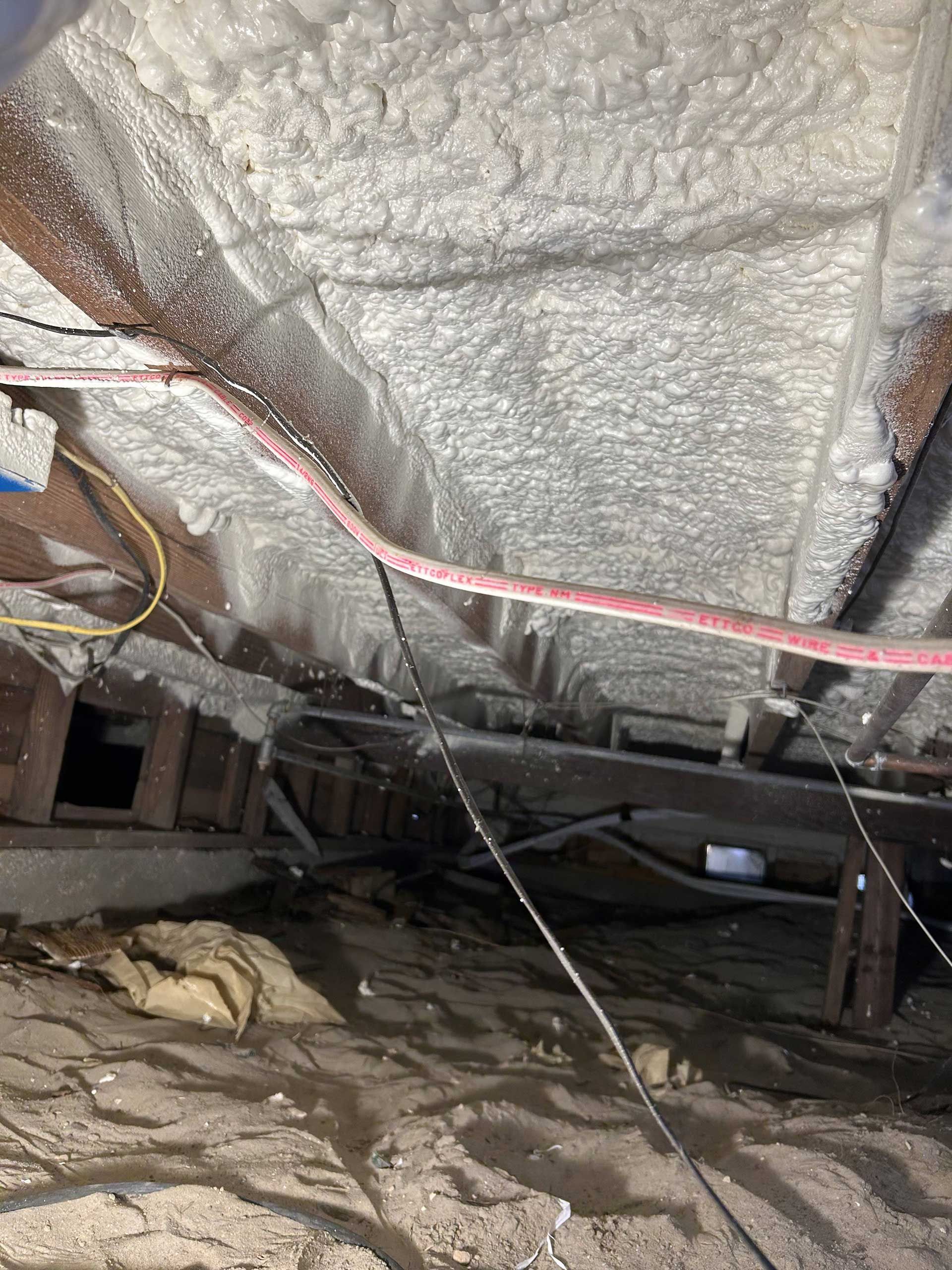 A view looking into a crawl space with spray foam insulation applied to the underside of the floor above.