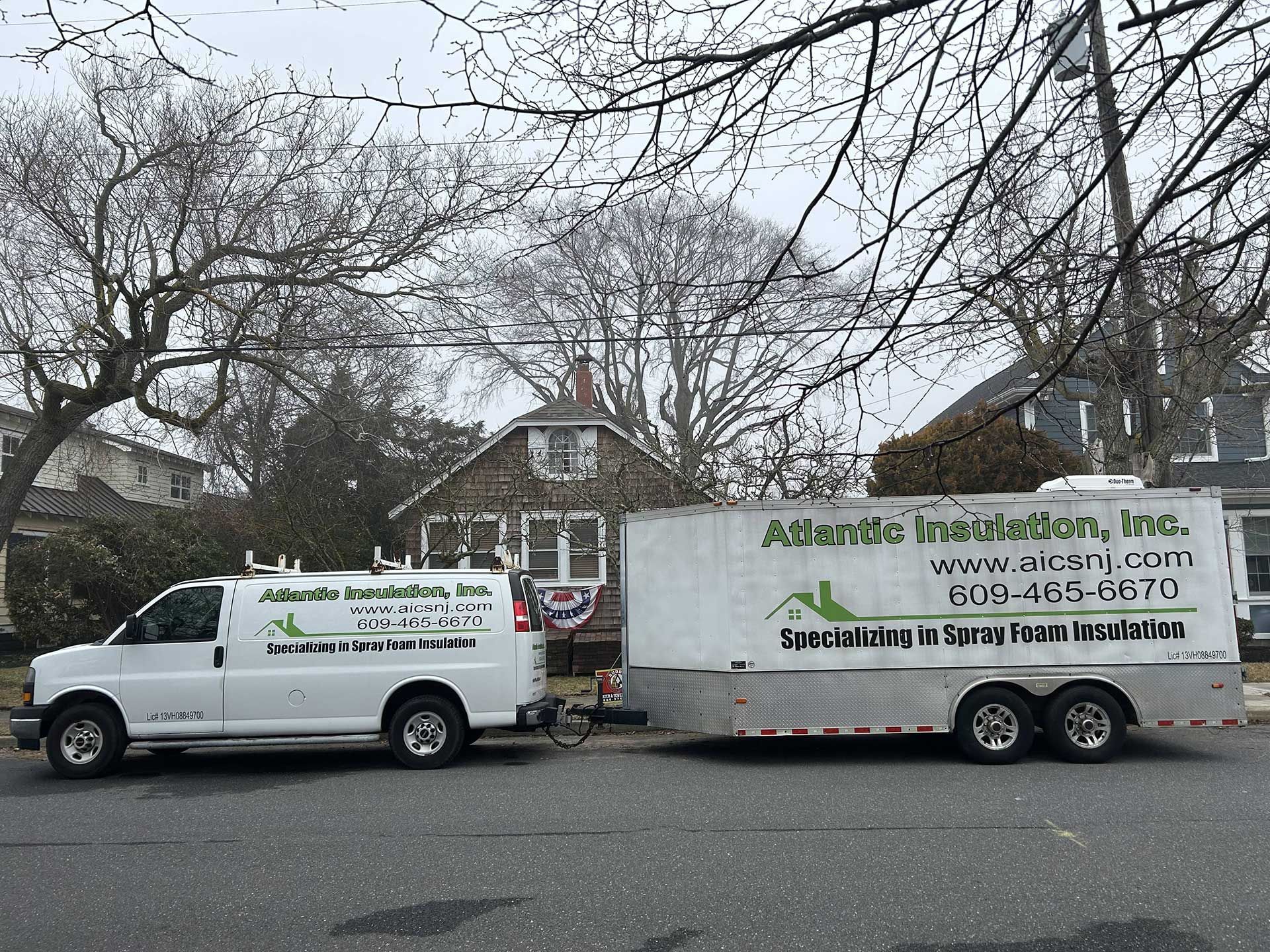A white Atlantic Insulation, Inc. service van towing a matching box trailer parked on a suburban street.