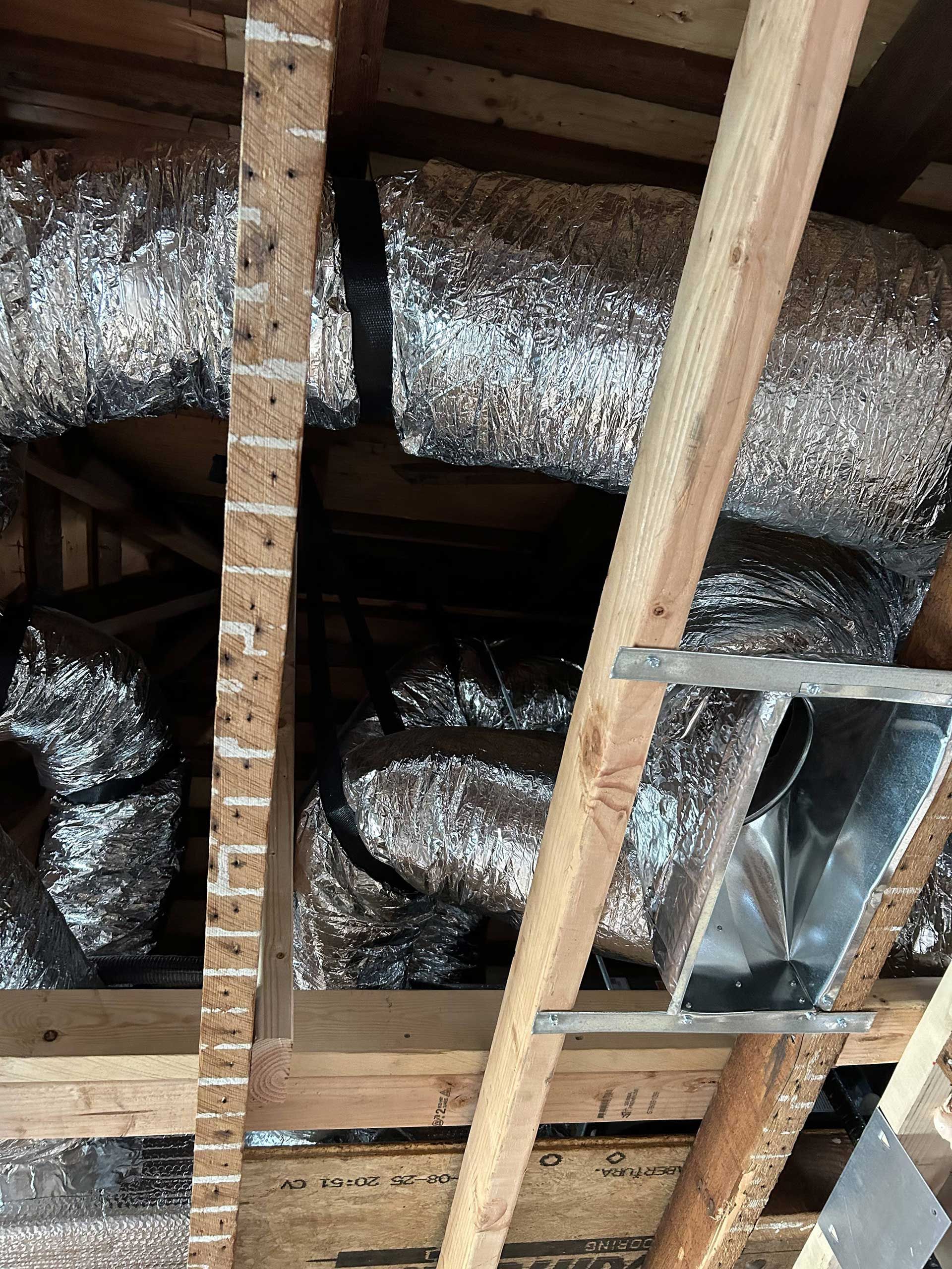 Insulated flexible ductwork and a rectangular metal HVAC vent boot installed between wooden ceiling joists in an attic.