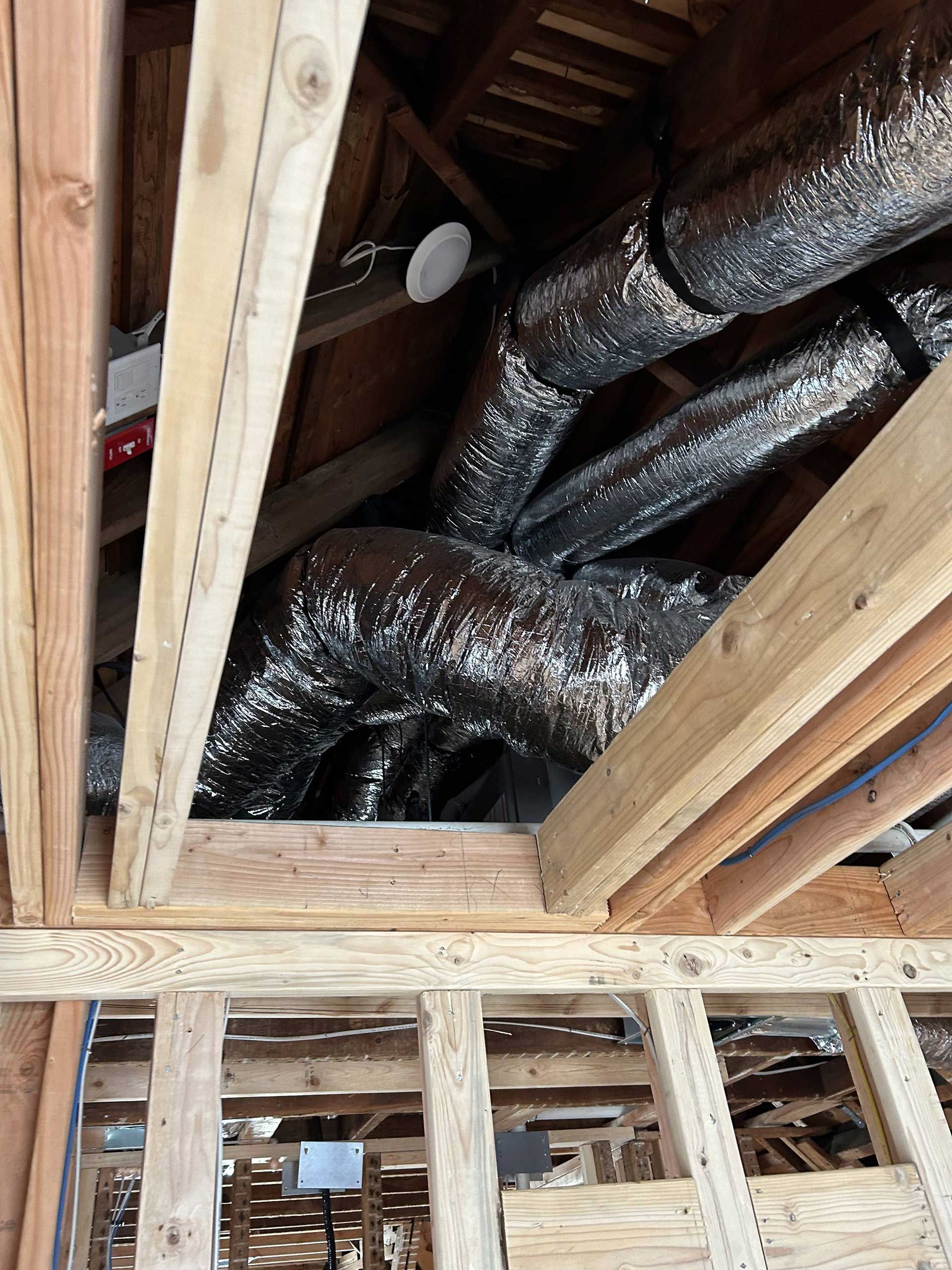 Flexible insulated HVAC ducts hanging between wooden ceiling joists in an unfinished construction space.