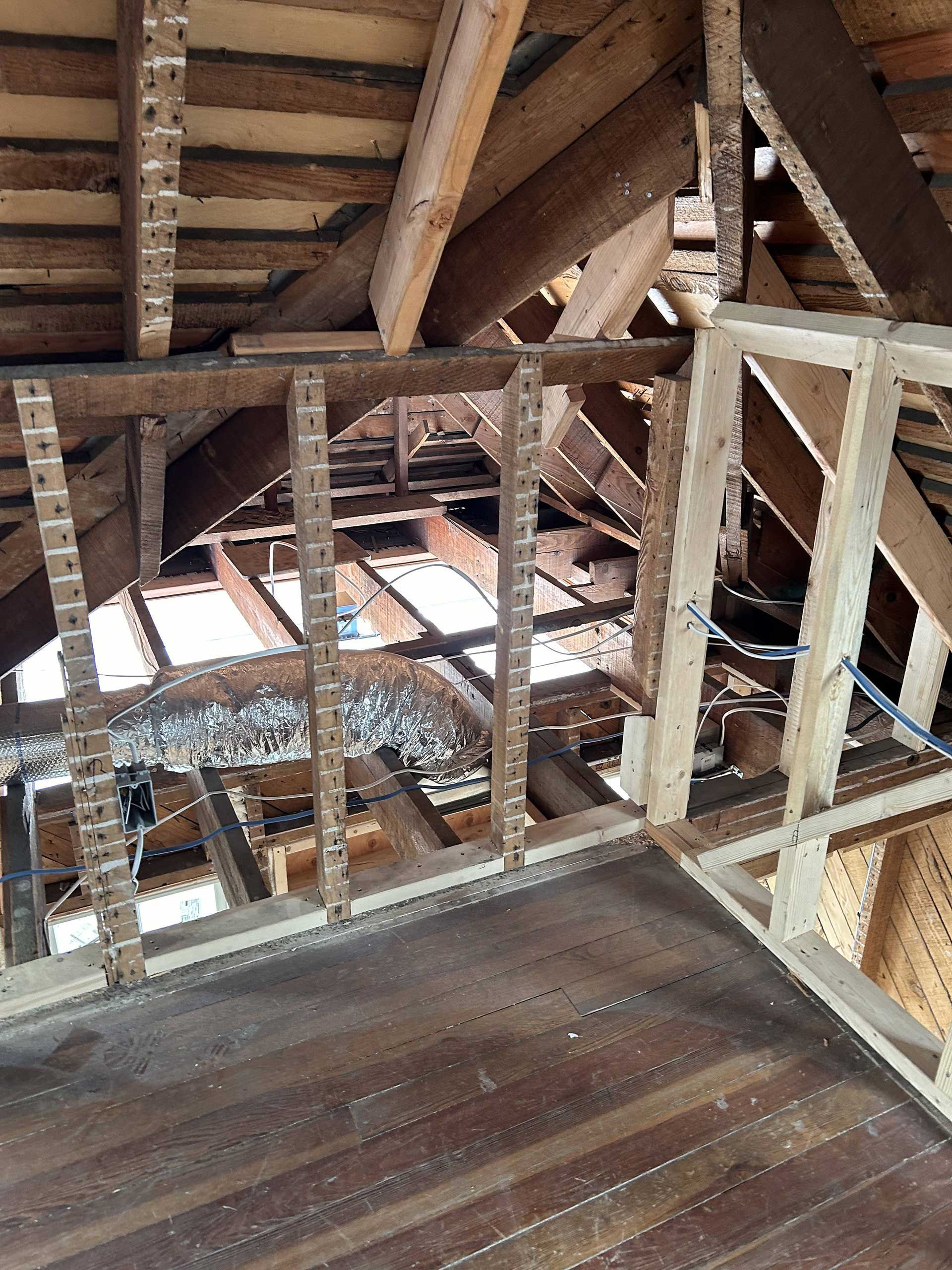 Attic interior showing old wooden roof rafters and a recently framed partition wall made of new light-colored lumber.