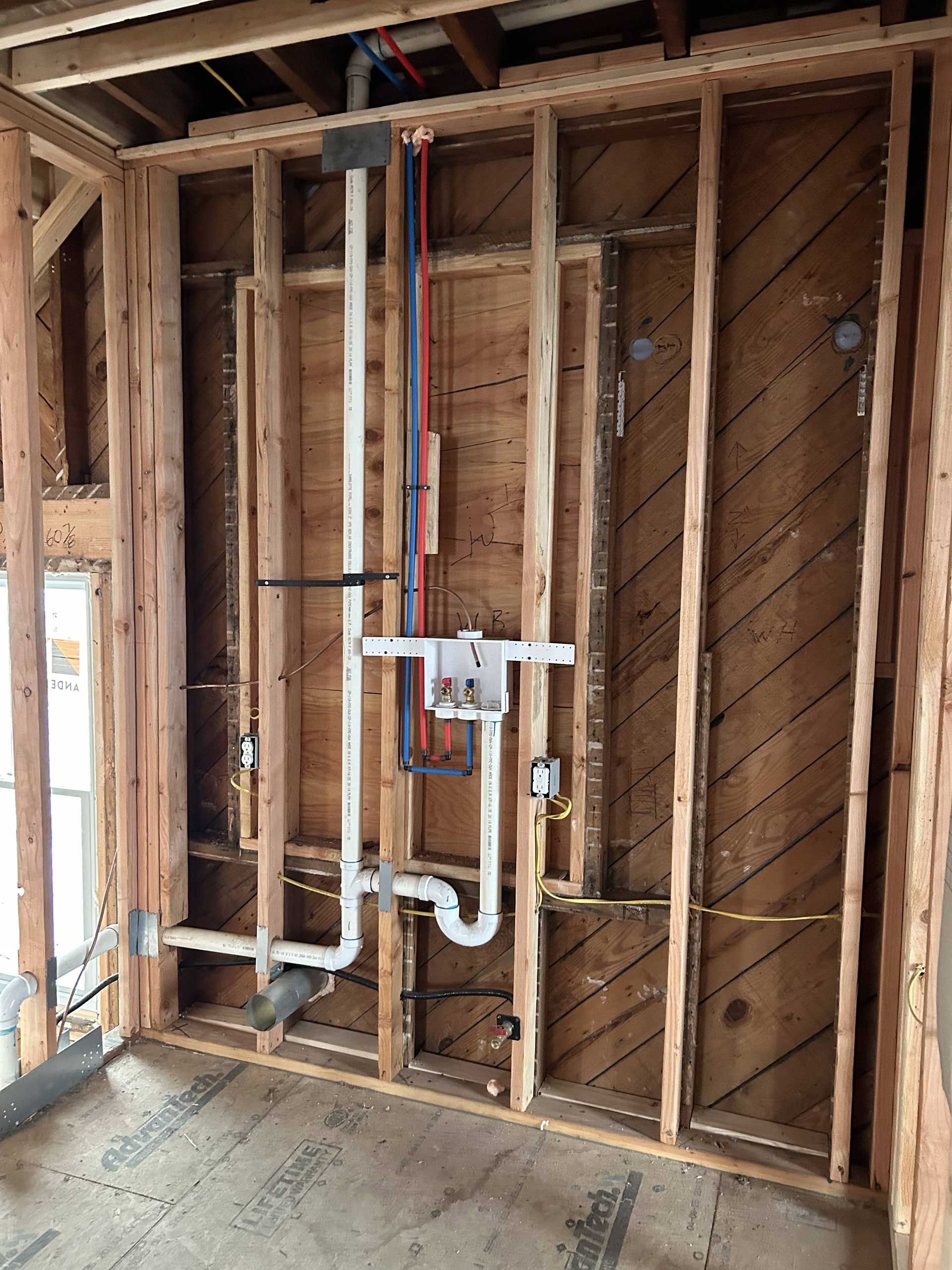 Wall studs with exposed plumbing pipes and a laundry box mounted in the center of the unfinished wooden frame.