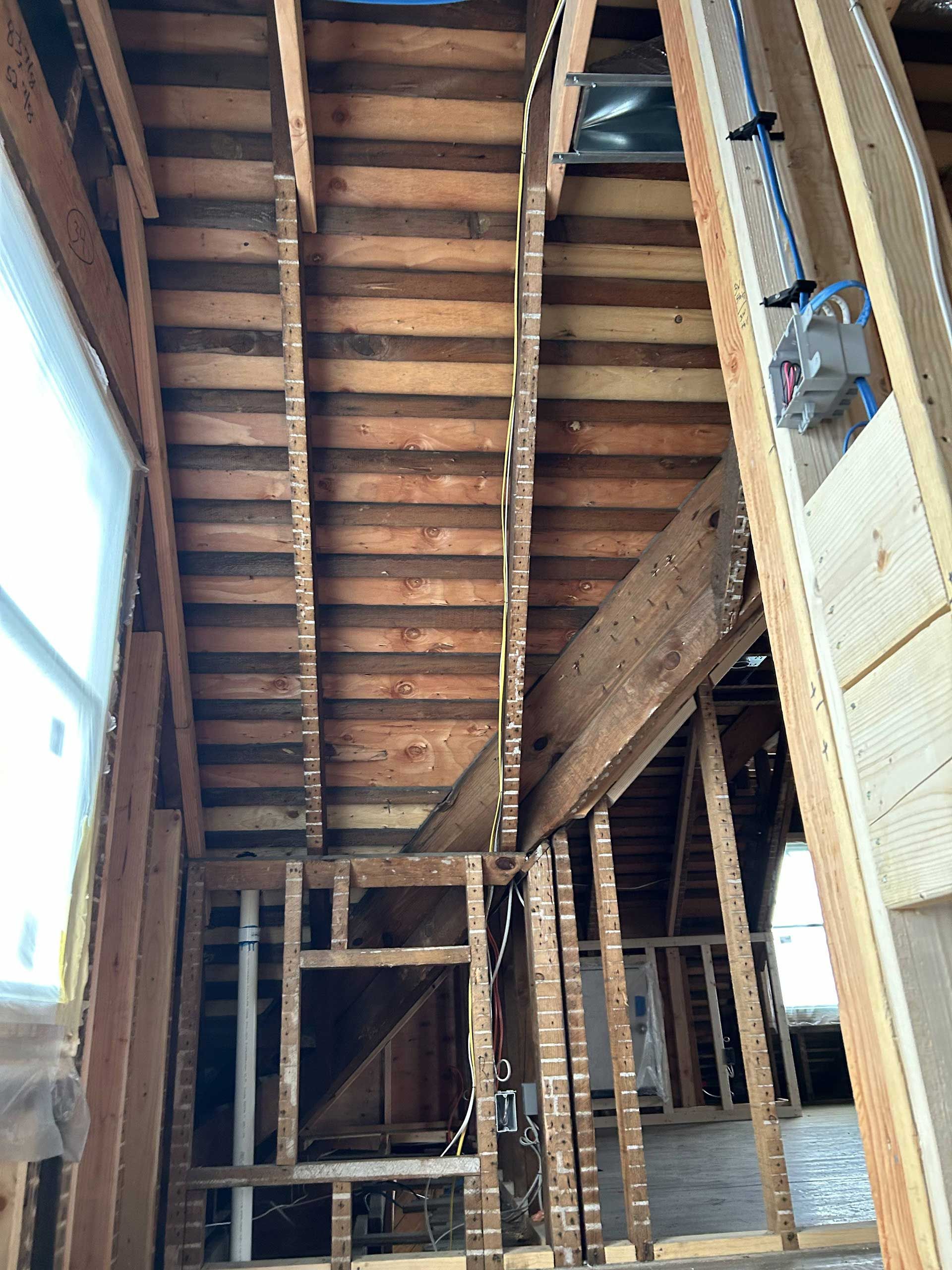 Unfinished wooden framing of a staircase under construction, with exposed beams and wiring visible in an open-stud room.