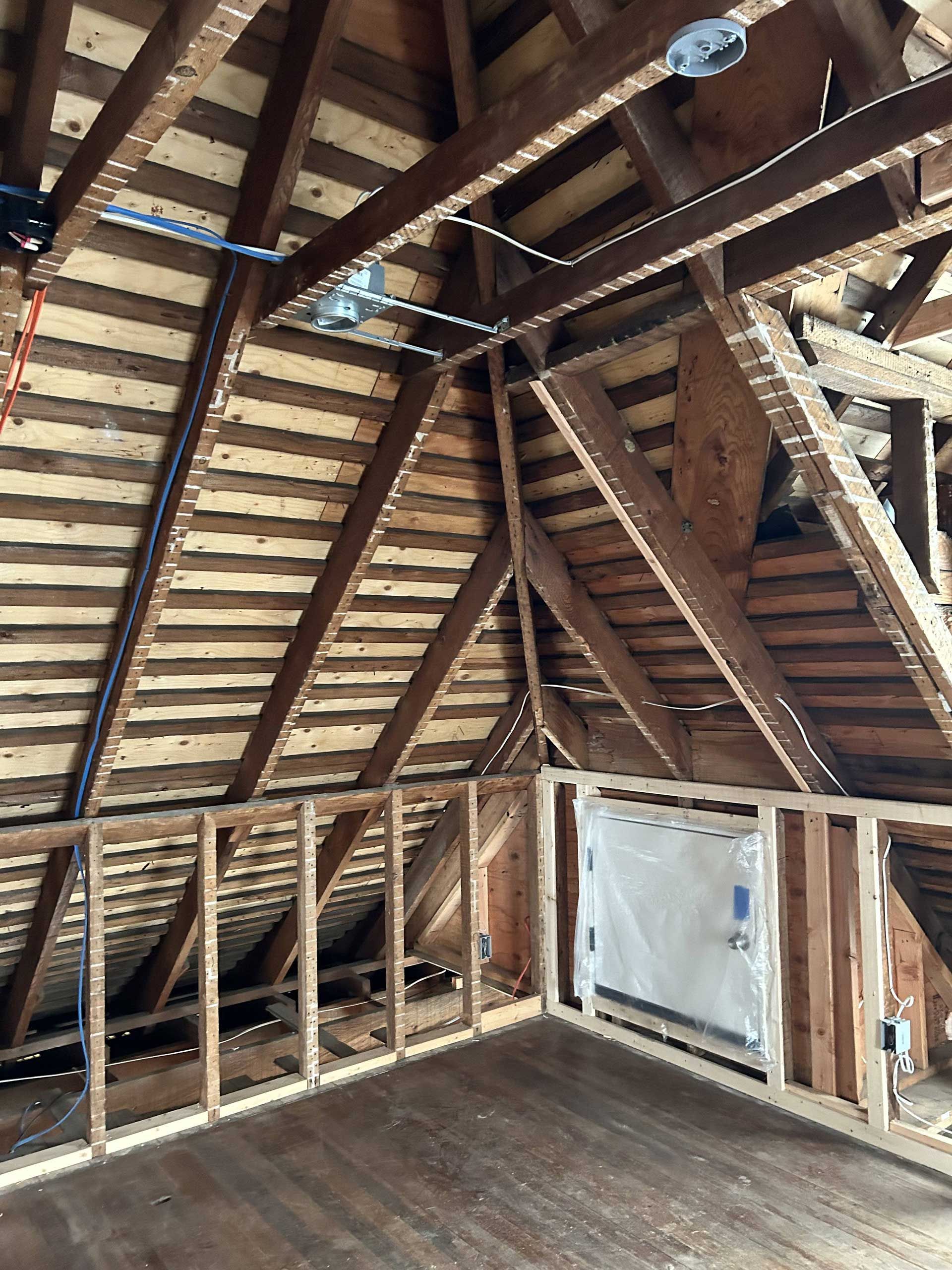 Attic under renovation with exposed wood framing, new wall studs, and electrical wiring in the rafters.