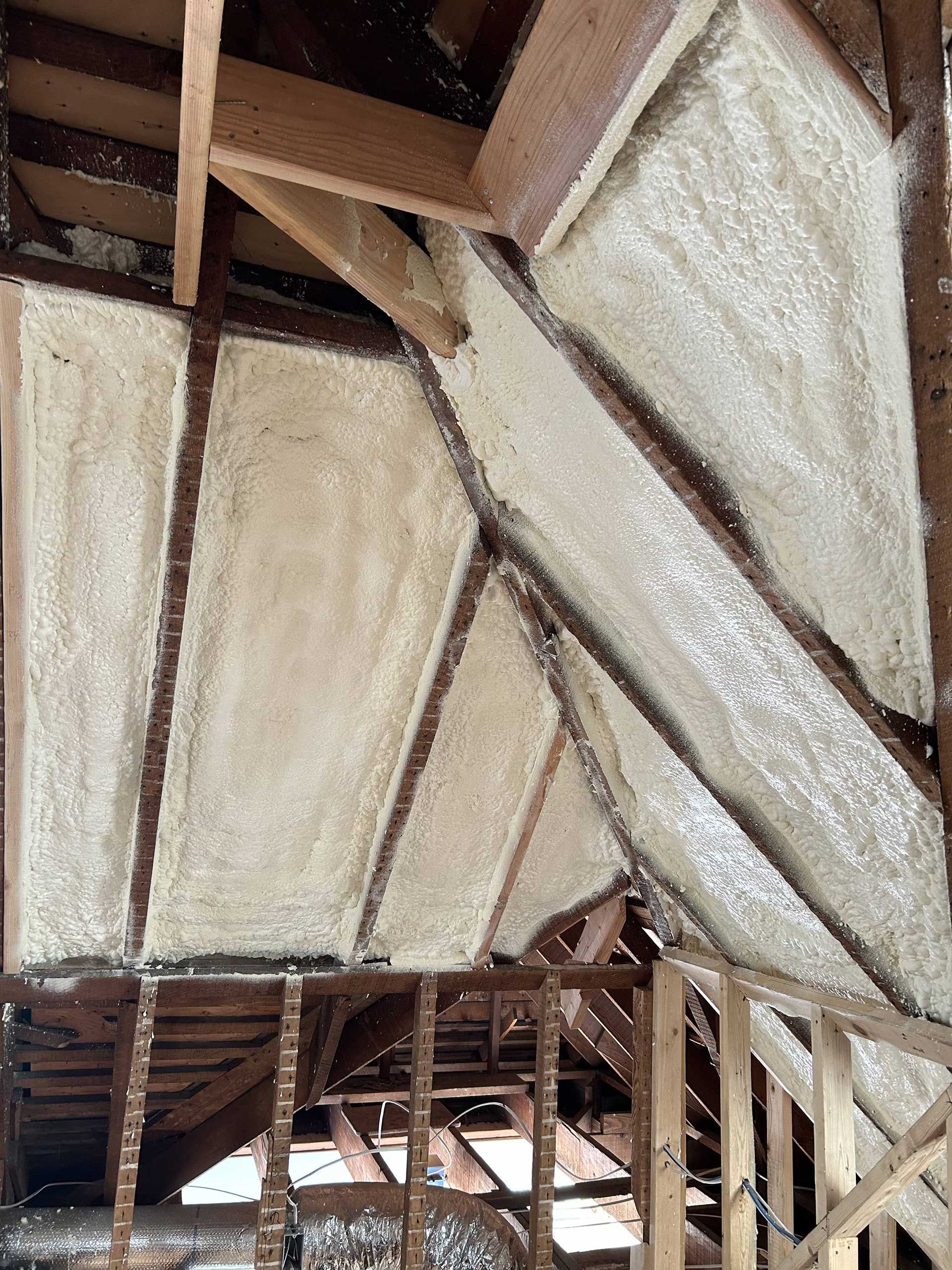 Spray foam insulation applied between wooden rafters and roof beams in a residential attic.