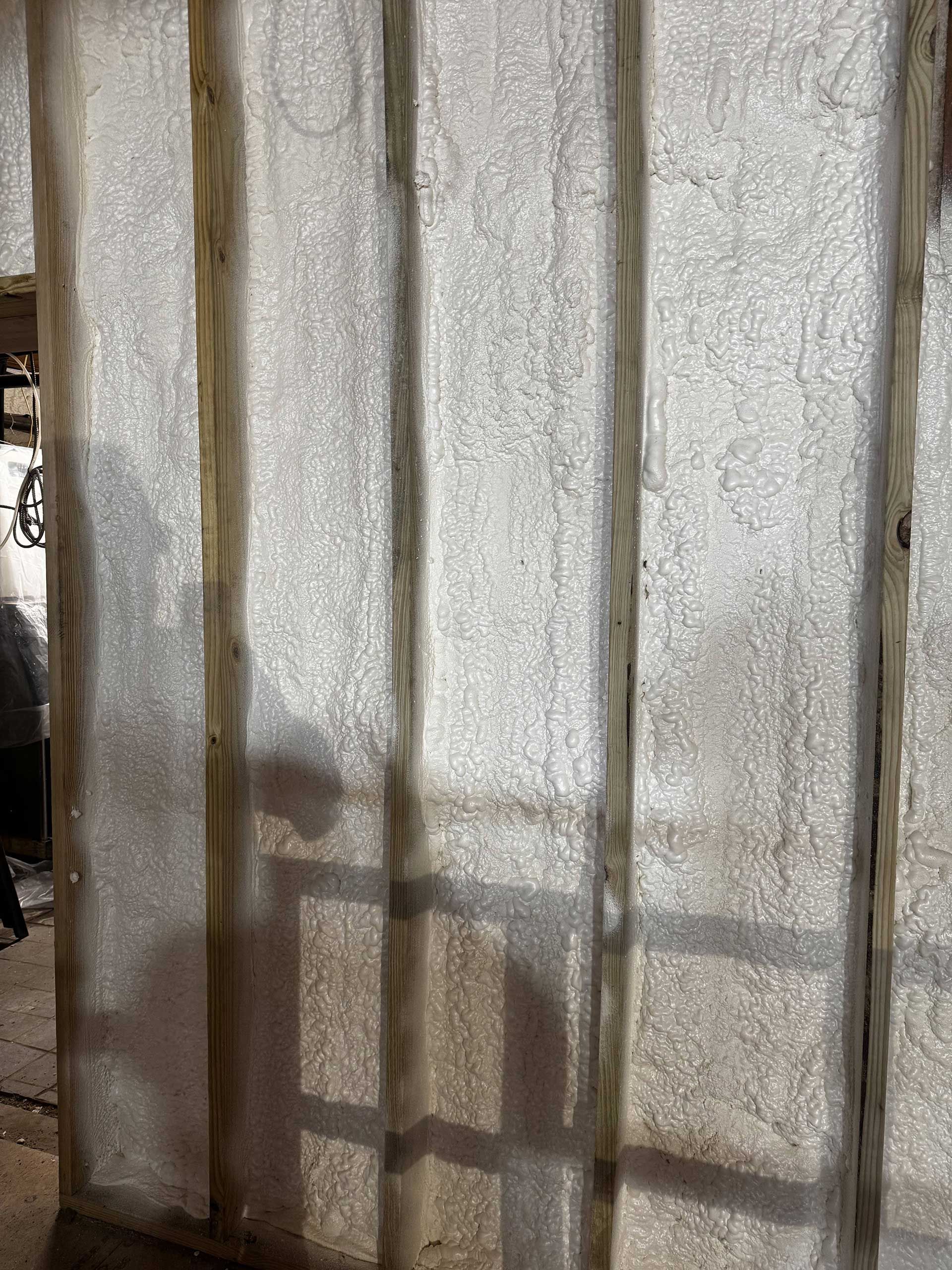 Light-colored foam insulation between vertical wooden wall studs, with shadows cast on the surface.