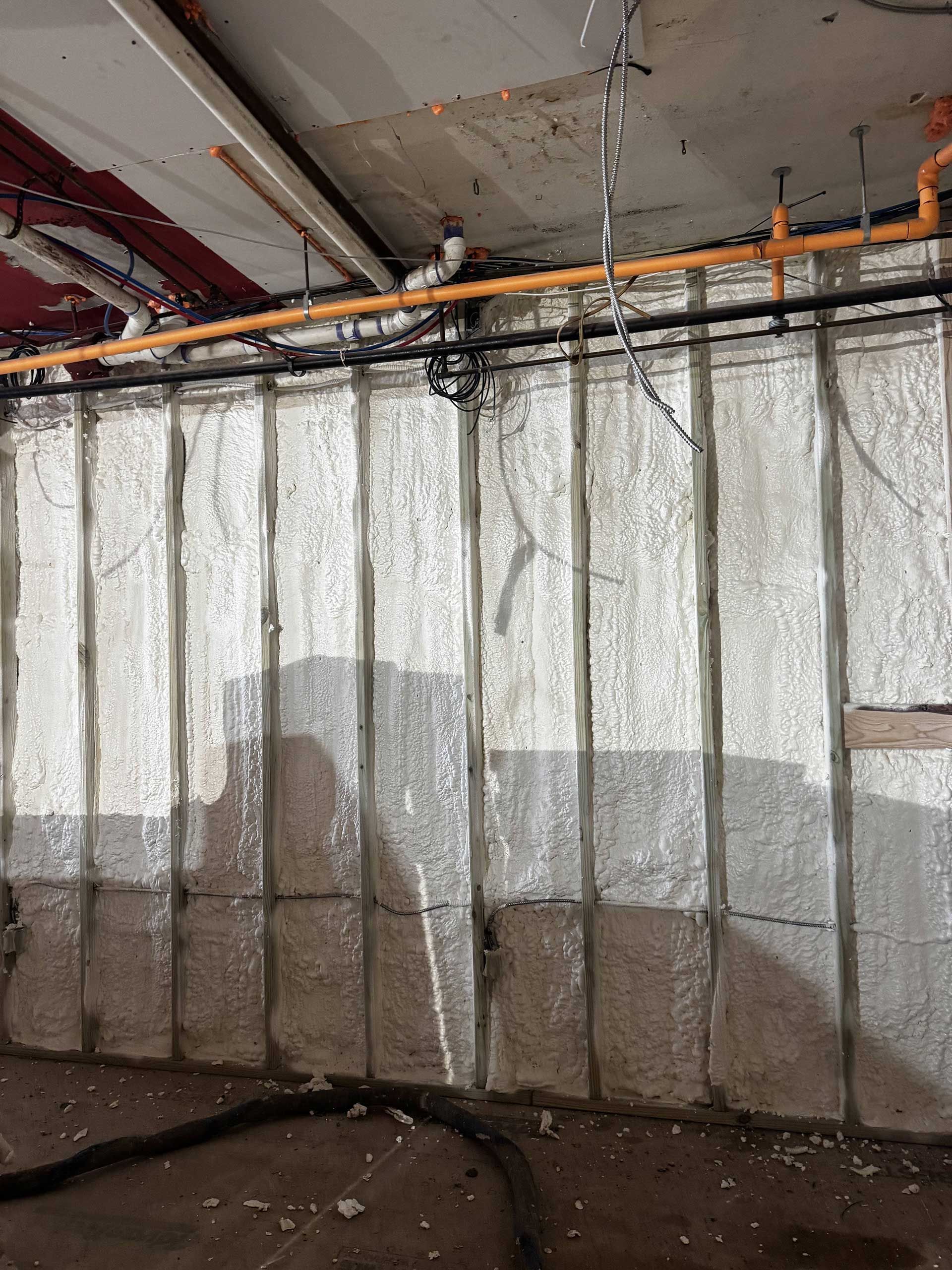 An interior view of a wall featuring foam insulation between metal studs, with visible water staining at the base.