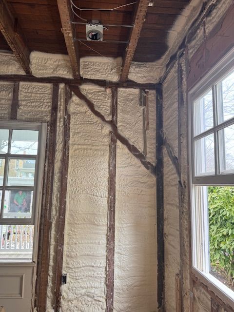 Interior view of a room with exposed wooden studs and spray foam insulation, near windows and a doorway.