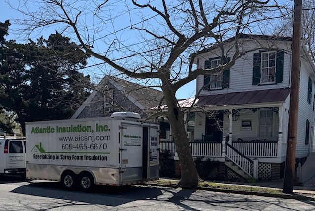 A white two-story house with a trailer from Atlantic Insulation parked on the street.