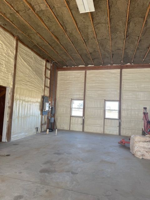 Interior view of a building with spray foam insulation on the walls and ceiling, and a concrete floor.