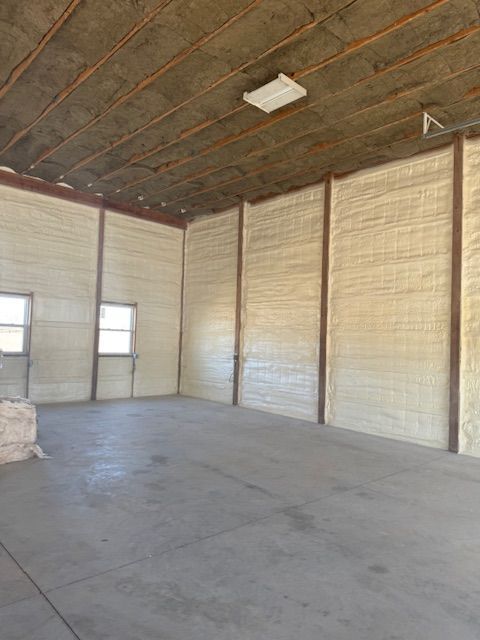 Interior of a warehouse with concrete floor, walls, and ceiling insulated with foam. Two windows are visible.