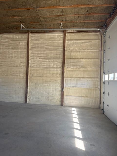 Interior of a building with spray foam insulation on walls and a concrete floor. Garage door on the right.