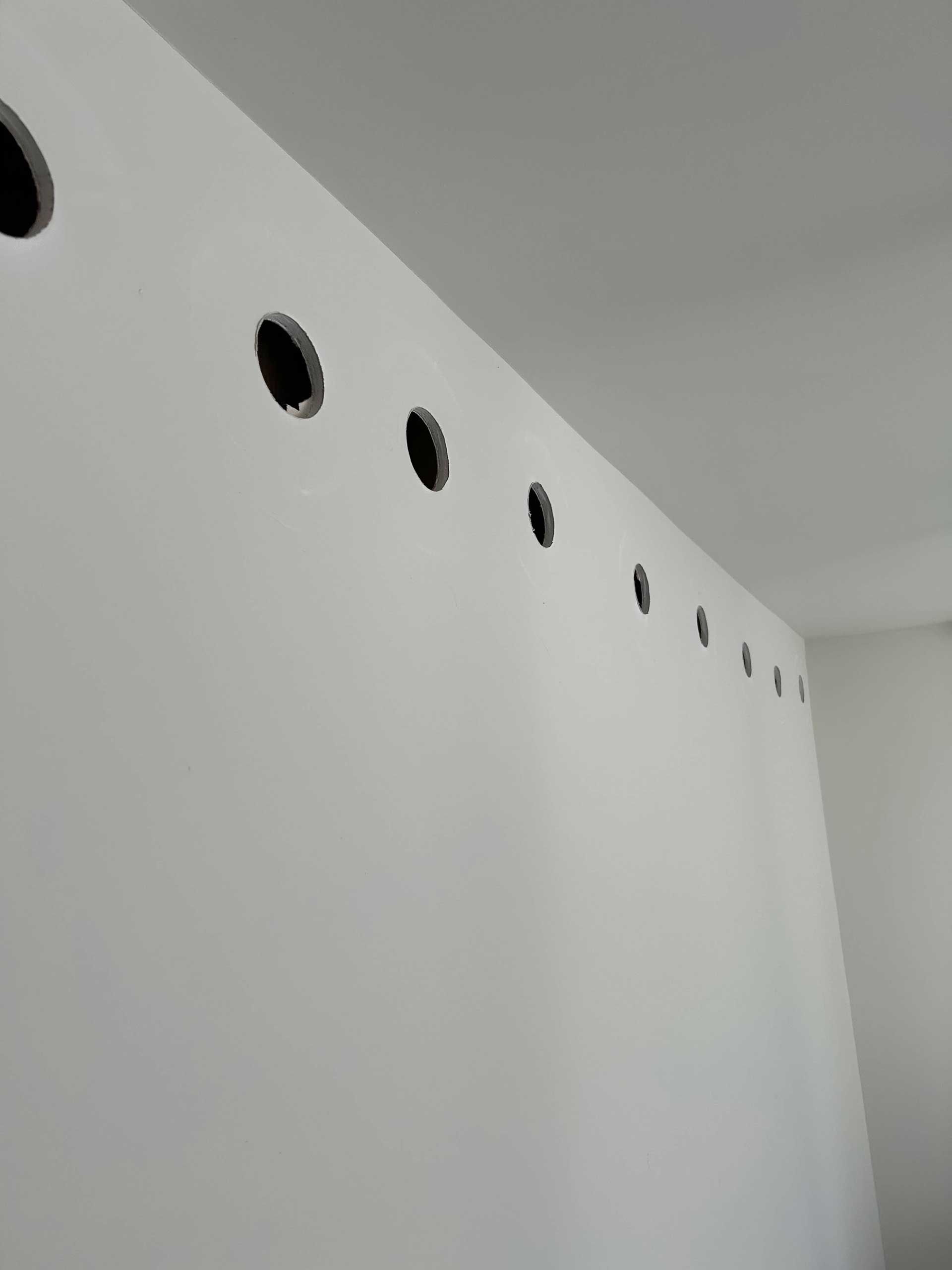 A white wall featuring a horizontal row of evenly spaced circular cutouts near the ceiling.