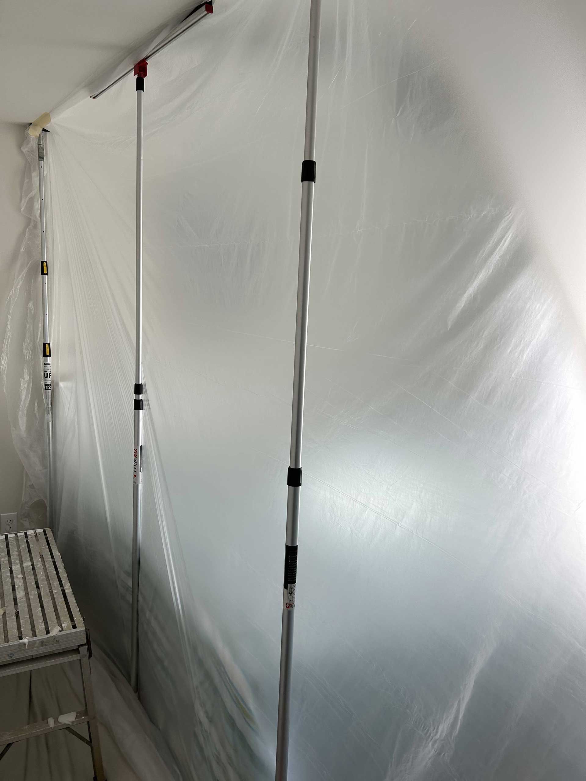 Plastic sheeting hung from the ceiling by adjustable poles to create a temporary dust partition in a room.