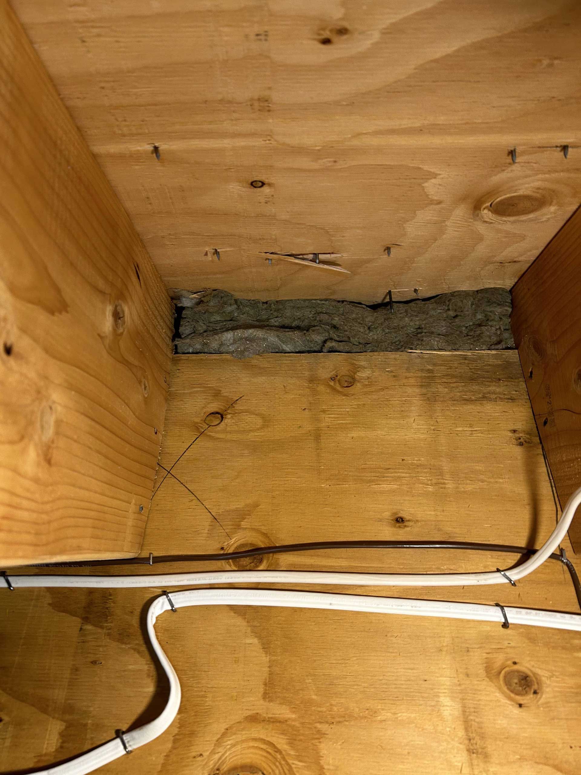 A top-down view of unfinished wooden framing in a building with a gap containing gray insulation and white wiring cables.