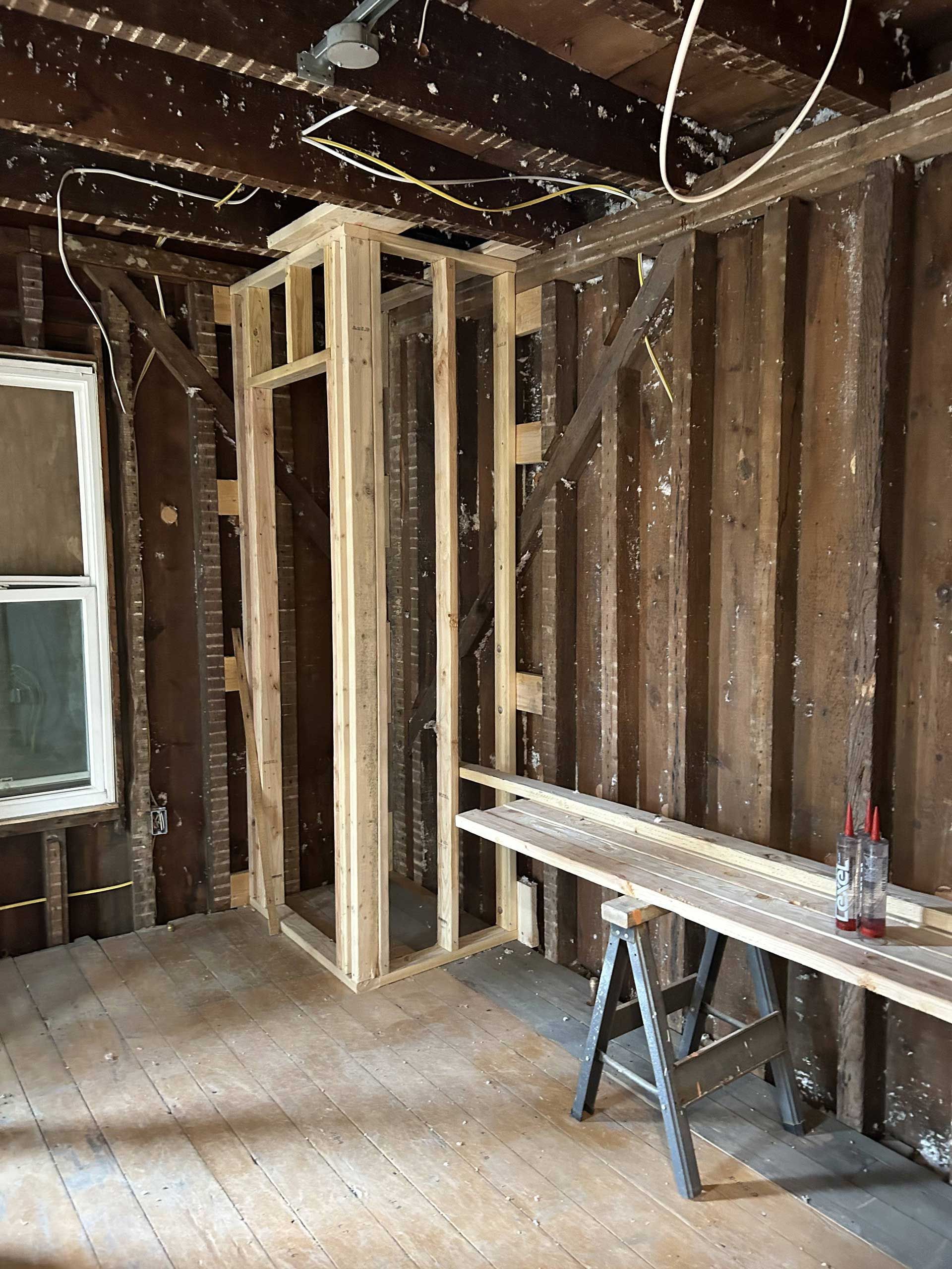 A room under renovation featuring new wooden wall framing for a doorway alongside exposed, dark timber wall studs.