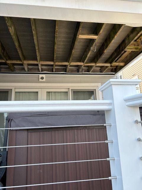 Covered patio with white railing and brown privacy screen under exposed roof beams