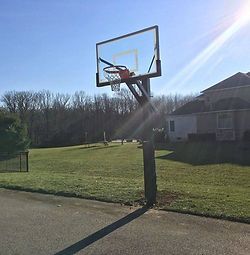 A basketball hoop is sitting on the side of a road next to a grassy field.