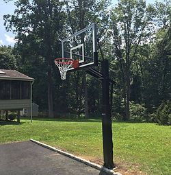 A basketball hoop is sitting in the middle of a driveway next to a house.