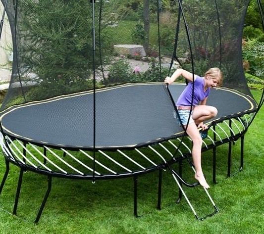 A girl is sitting on a trampoline with a ladder attached to it