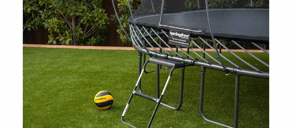 A trampoline is sitting on top of a lush green lawn next to a volleyball.