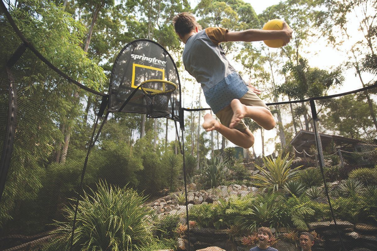 A man is jumping in the air while playing basketball on a trampoline.