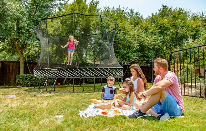 A family is sitting on the grass in front of a trampoline.