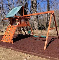 A wooden swing set with a climbing wall and swings in a park.