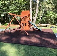 A wooden playground with a slide and swings in a backyard.