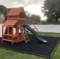 A wooden playground with a slide and stairs in a backyard.