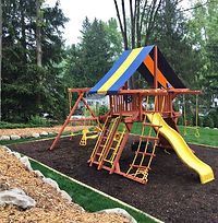 A wooden playground with a blue , yellow and orange roof and a yellow slide.