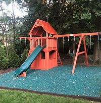 A red playground set with a slide and swings in a backyard.