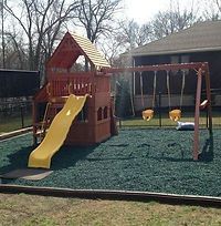 A wooden playground with a yellow slide and swings in a backyard.
