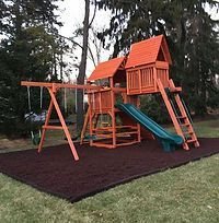 A wooden playground set is sitting on top of a rubber mat in a backyard.