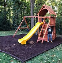 A man is standing in front of a wooden playground with a yellow slide.
